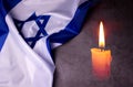 Holocaust Remembrance Day. Yom HaShoah. Bright Burning Candle and the official flag of Israel on a dark grey background.