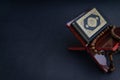 Holy Al Quran with written arabic calligraphy meaning of Al Quran and tasbih or rosary beads on black background