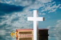 Holy bible and white cross against blue clouded sky. On a reflective surface Royalty Free Stock Photo