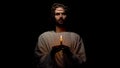 Holy man in crown of thorns holding candle in darkness Jesus before resurrection