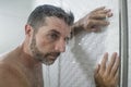 Home bathroom dramatic portrait of young attractive sad and depressed man in the shower leaning against the wall thoughtful Royalty Free Stock Photo