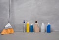 Home cleaning products and tools. Broom, bottles with different detergents standing on the floor against grey wall Royalty Free Stock Photo