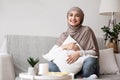 Smiling Muslim Woman In Hijab Sitting On Sofa And Cuddling Pillow