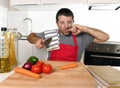 Home cook man in red apron slicing carrot with kitchen knife suffering domestic accident cutting hurting finger