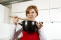 Home cook woman at kitchen holding cooking pot and spoon tasting soup in a funny disgusting bad taste face