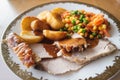 Home cooked pork roast dinner with crackling, gravy, roast potatoes and vegetables on a white plate with a gold trim Royalty Free Stock Photo