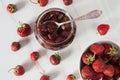 Jam from fresh juicy sweet organic strawberries in a glass jar with a spoon close-up on a light marble background. Royalty Free Stock Photo
