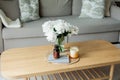 Home cozy interior. Candles, a bouquet of peonies in a glass vase on a wooden coffee table. Spring