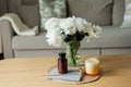 Home cozy interior. Candles, a bouquet of peonies in a glass vase on a wooden coffee table. Spring