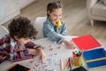 Curly boy and dark-haired girl sitting at round table, playing with alphabet letters, smiling Royalty Free Stock Photo