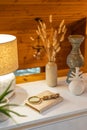 Home decoration concept. Various vases with dry wheat, a yellow lamp on a white chest of drawers in a wooden room