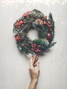 Home decoration for winter holidays. Female hand carefully touches a Christmas wreath on white background with lights, wooden top Royalty Free Stock Photo