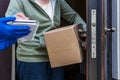 Home delivery, a courier in gloves in front of the open door of the house passes the parcel to the woman who signs for Royalty Free Stock Photo