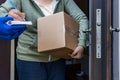 Home delivery, a courier in gloves in front of the open door of the house passes the parcel to the woman who signs for Royalty Free Stock Photo