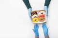 Home delivery of sweets during COVID-19 epidemic. Courier in rubber gloves gives box of delicious donuts with glaze and