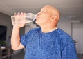 Home, fitness or senior man drinking water for wellness, hydration or exercise recovery in retirement. Training, fatigue
