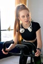 redhead female working out at home on the exercise bike, young female cycling for good health.