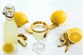 Home ginger tincture in a glass and fresh lemons on the white wooden background