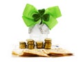 Home with glitter on stack of coins and banknotes and green bow with shamrock on white background. High value cost of property in