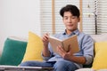 At home, a handsome young Asian businessman in casual clothing reads a book on the couch Royalty Free Stock Photo