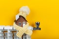 Home heating radiator. A model of a house wrapped in a scarf and a hat on a radiator indoors against a yellow wall. Royalty Free Stock Photo