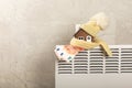 Home heating radiator. Model of a house wrapped in a scarf and hat on a radiator indoors against a gray wall. Royalty Free Stock Photo