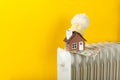 Home heating radiator. A model of a house wrapped in a scarf and a hat on a radiator indoors against a yellow wall. Royalty Free Stock Photo