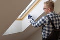 Home improvement concept, handyman painting a wall with a white paint near roof window in attic