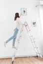 woman on ladder decorating home with art