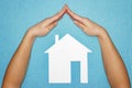 Home insurance concept. Hands in form of roof over house of white paper on blue background