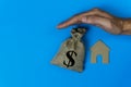 Home insurance concepts. House protect. A man hand protected a small house and money bag over a roof on blue background Royalty Free Stock Photo