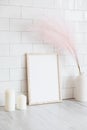 Home interior design. Photo frame mockup, candles, pink dried flowers in vase on table. Brick tiles wall on background. Royalty Free Stock Photo