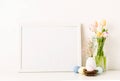 Mockup with a white frame spring tulips in vase, gypsophila and pastel colored eggs on light background Royalty Free Stock Photo