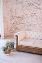 Home interior with a white quilted sofa with wooden base in front of a blank brick wall