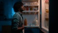 Home kitchen at night dark room hungry Hispanic man Indian male guy want eat rubbing belly open fridge searching food Royalty Free Stock Photo