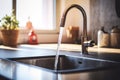 Home kitchen sink and water flowing from faucet, sunlit window in background