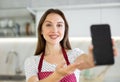 At home in kitchen smiling woman in apron shows blank smartphone screen close up. Dark touch screen workspace