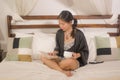 Home lifestyle morning portrait of young beautiful and happy Asian Chinese woman in nightgown reading a book in bed enjoying the Royalty Free Stock Photo