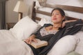 Home lifestyle morning portrait of young beautiful and happy Asian Korean woman in nightgown reading a book in bed enjoying the Royalty Free Stock Photo