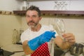 Home lifestyle portrait of happy and attractive man in red apron smiling at kitchen washing dishes and wine glass doing housework Royalty Free Stock Photo