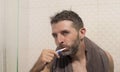 Home lifestyle portrait of young attractive and happy man with towel on his neck brushing his teeth in the bathroom relaxed and Royalty Free Stock Photo