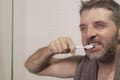 Home lifestyle portrait of young attractive and happy man with towel on his neck brushing his teeth in the bathroom relaxed and Royalty Free Stock Photo