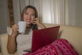 Young attractive and natural Asian Indonesian woman in pajamas pants smiling relaxed on couch networking using laptop computer Royalty Free Stock Photo