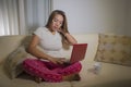 Young attractive and natural woman in pajamas pants relaxed on couch networking using laptop computer shopping online or working Royalty Free Stock Photo