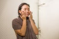 Young beautiful and happy Asian Korean woman applying serum facial skin care and face treatment in the bathroom enjoying morning