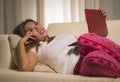 Young beautiful and natural Asian Indonesian woman in pajamas pants relaxed on couch networking using laptop computer shopping Royalty Free Stock Photo