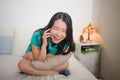 Home lifestyle portrait of young happy and attractive Asian Korean woman sitting on bed talking on mobile phone with girlfriend Royalty Free Stock Photo