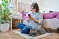 Female sitting on floor using smartphone, pet cat lying near owner