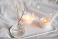 Home liquid fragrance in glass bottle and burning candles staying on white ceramic tray in bed close up. Royalty Free Stock Photo