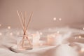 Home liquid fragrance in glass bottle and burning candles staying on white ceramic tray in bed close up. Royalty Free Stock Photo